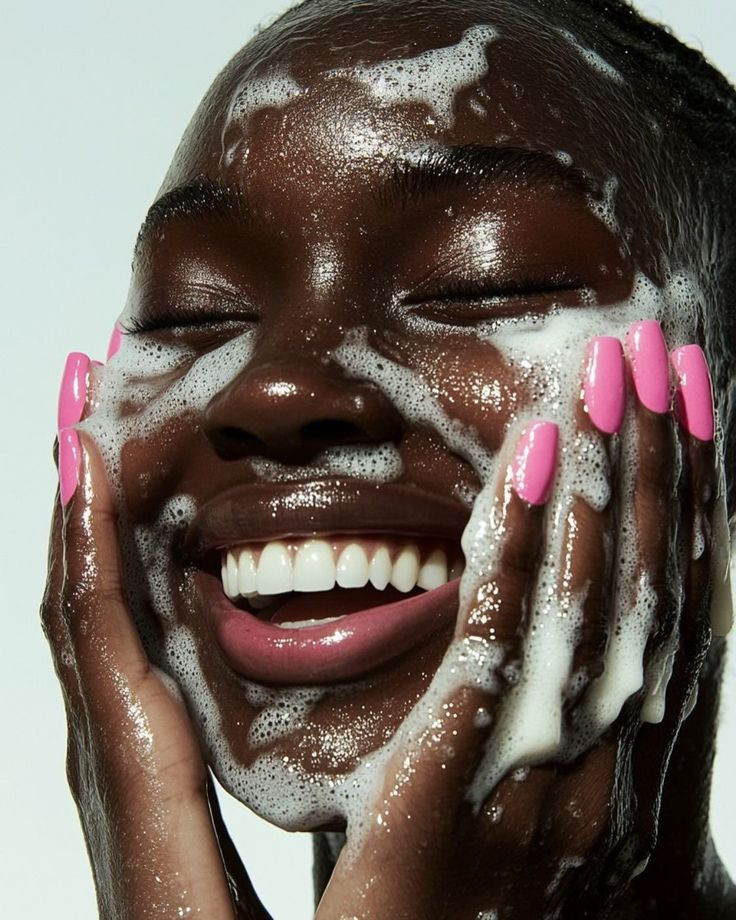 Close-up of a woman laughing while washing her face with cleansing foam
